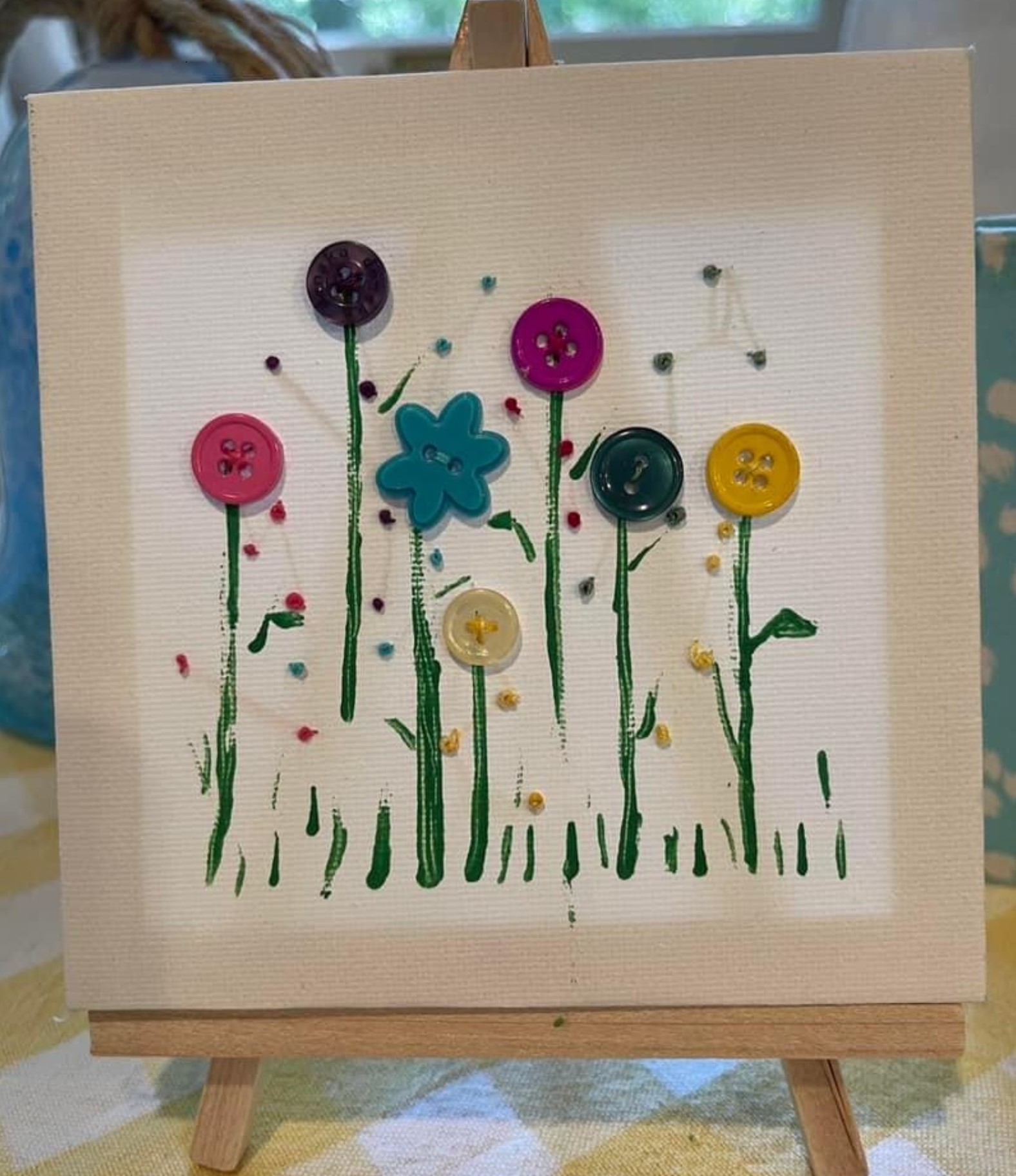 canvas displayed on an easel with colorful flowers made using buttons