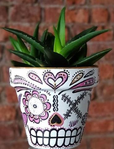 flower pot painted to look like a sugar skull with a green plant inside of it